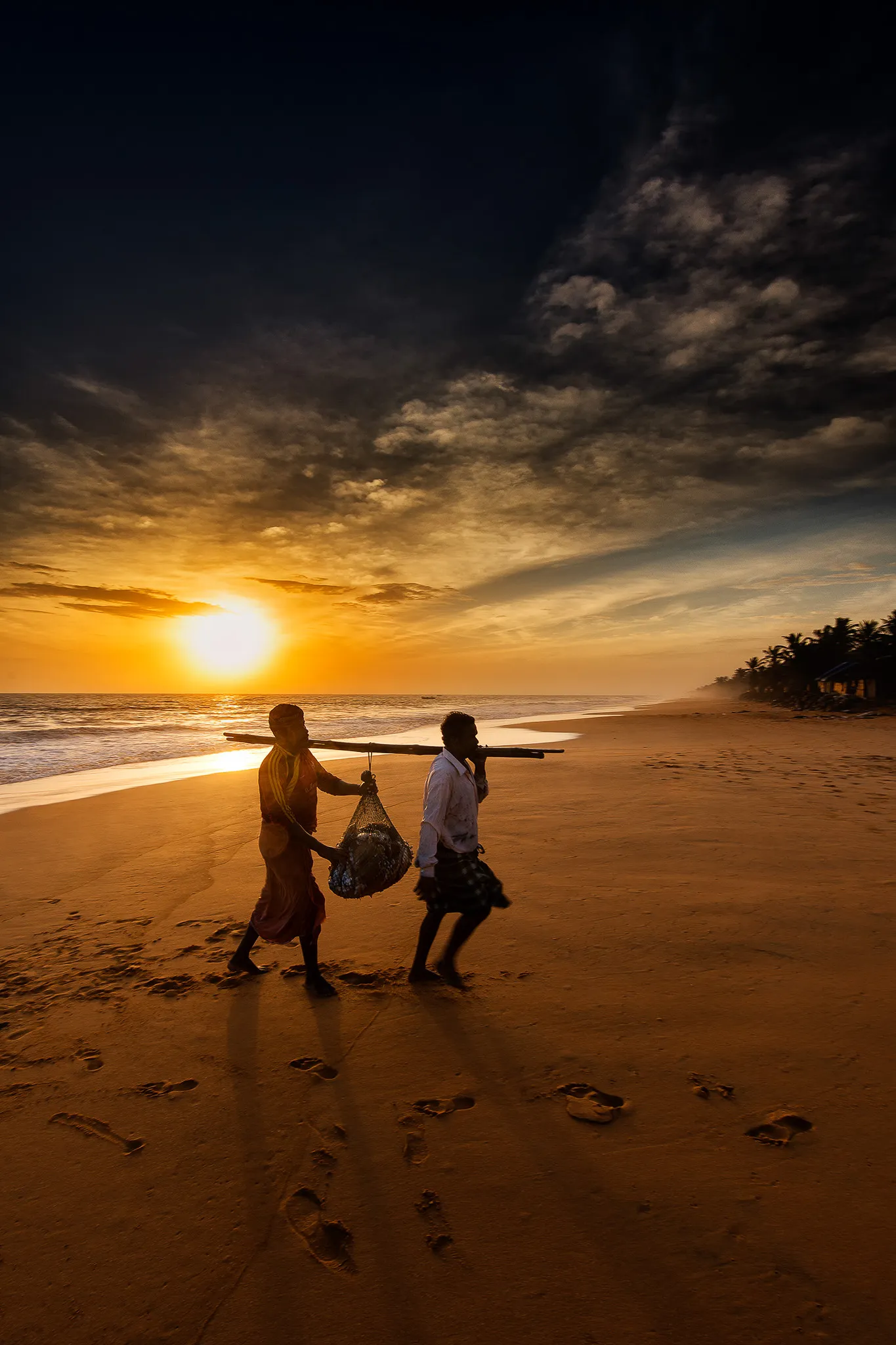 Two fishermen walking beach at sunset