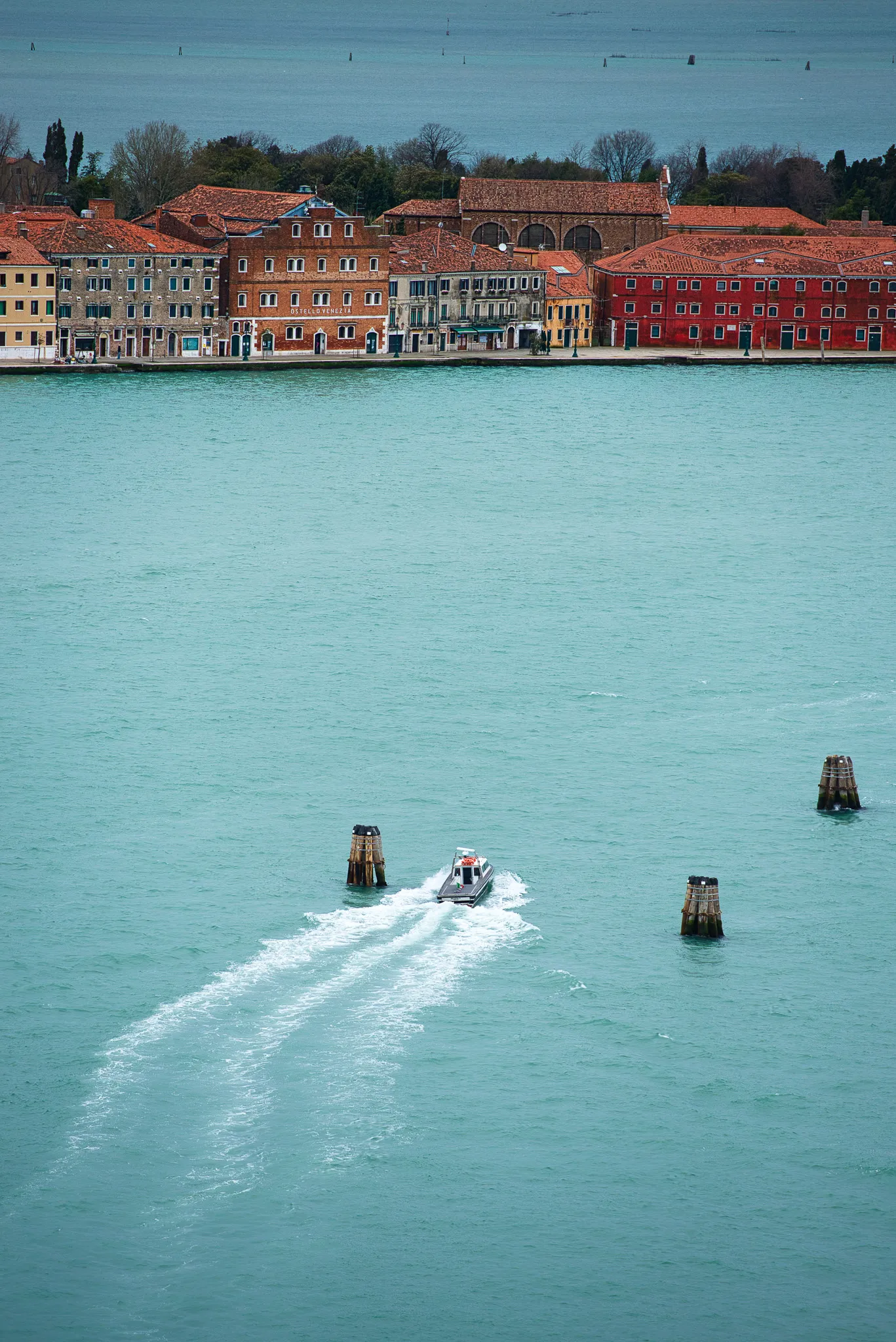 A small motorboat crossing the turquoise Venice lagoon with colourful buildings on the far shore